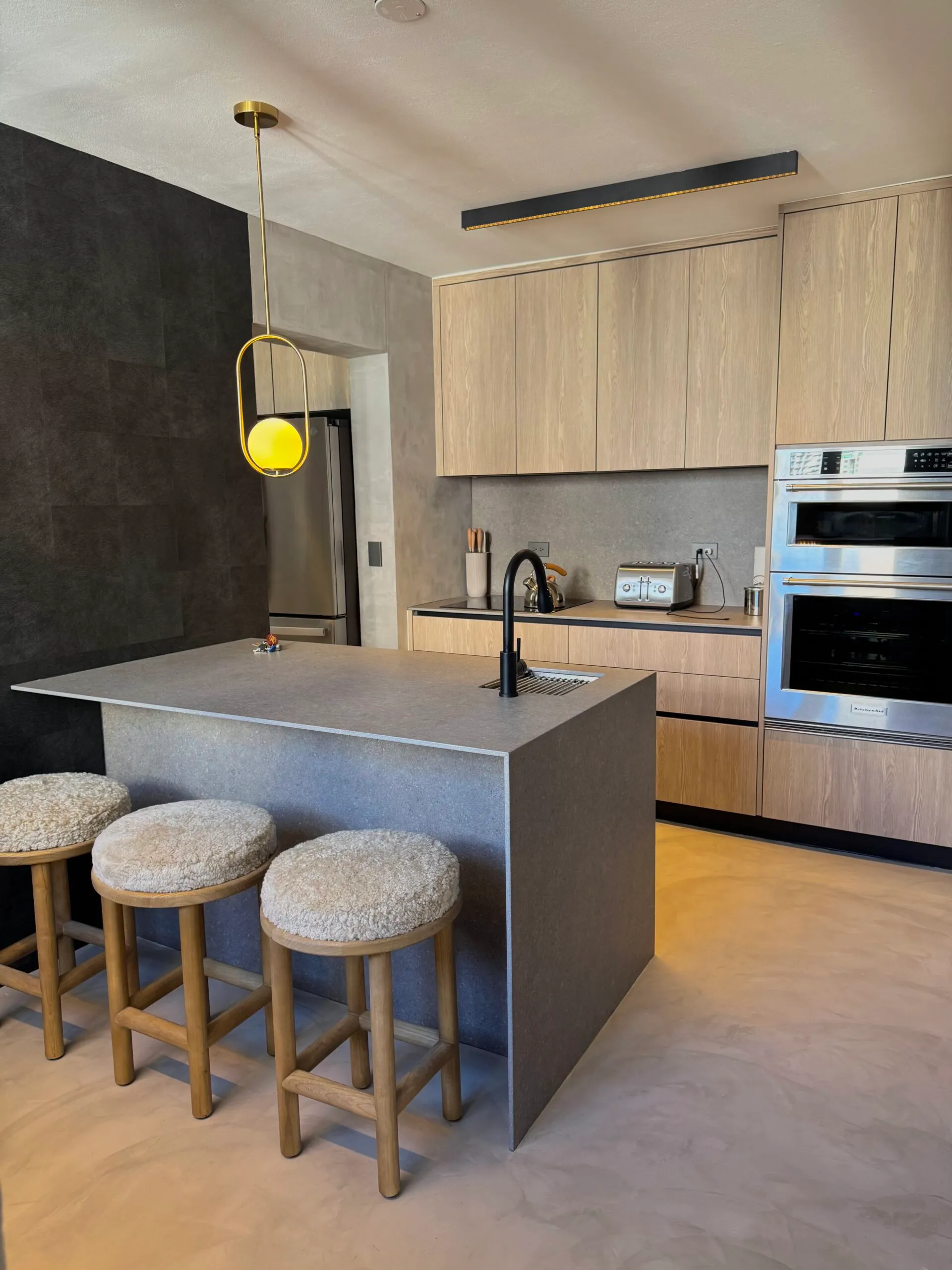 Kitchen with a seamless microcement floor and walls, oak cabinetry and a stone island.